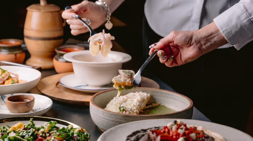 Hands serving various dishes, including a salad, a ceviche, and a main course with cheese.