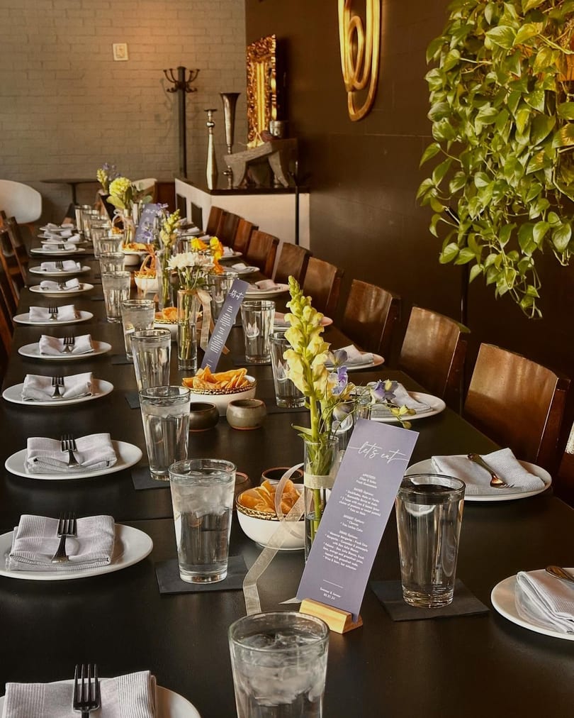 A long dining table set for a private event with place settings, flowers, and menus.