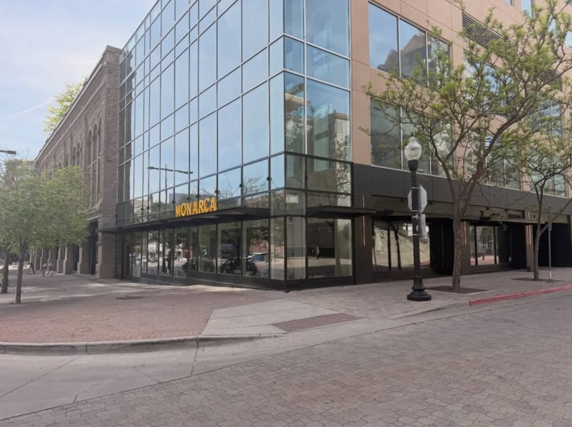 Exterior view of Monarca restaurant, a modern building with large glass windows and a brick sidewalk.